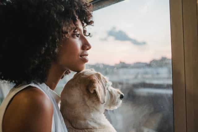 Vrouw kijkt met hond uit het raam